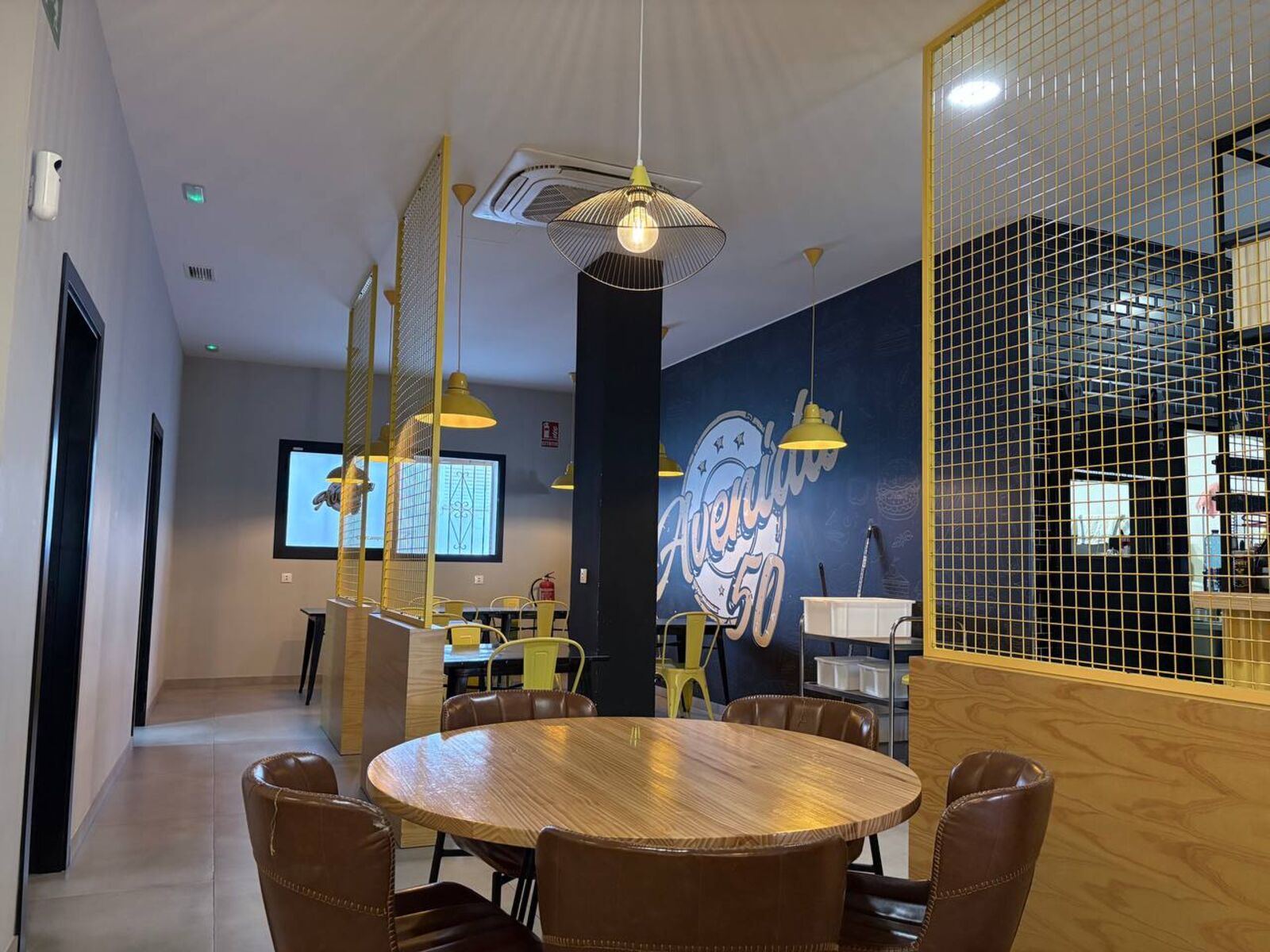 Comedor con separadores de rejilla amarilla, lámparas mostaza y mural azul con el logo