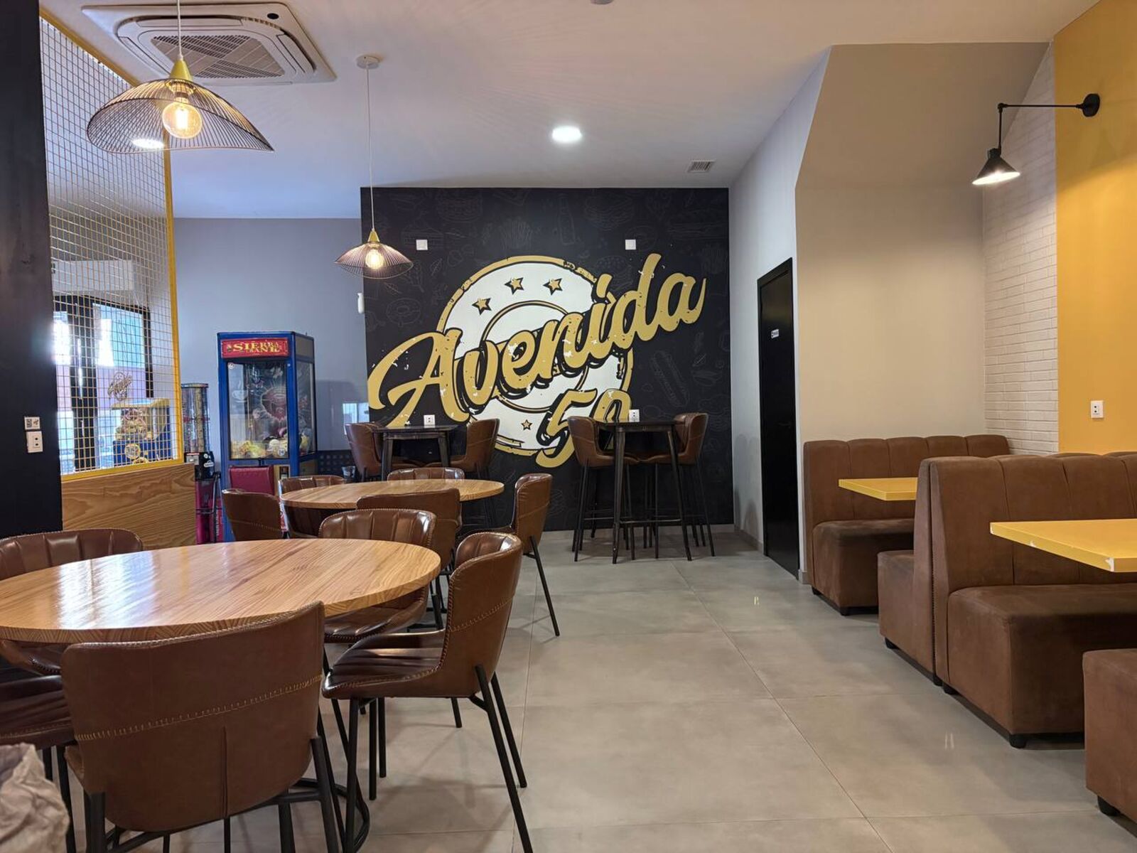 Salón de Avenida 50 con mesas redondas de madera, sofás marrones y el mural al fondo
